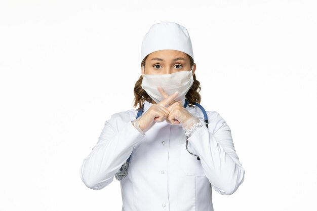 Front view young female doctor with sterile mask and gloves due to coronavirus on white surface