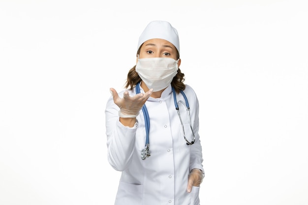 Front view young female doctor with sterile mask and protective gloves due to coronavirus on white desk