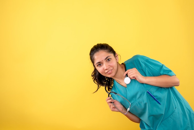 Foto gratuita vista frontale del giovane medico femminile con lo stetoscopio sulla parete gialla