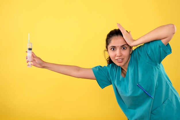 Front view of young female doctor with syringe holding head on yellow wall