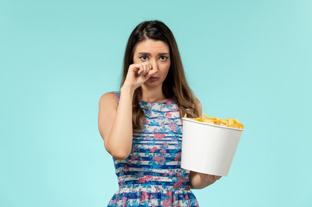 Вид спереди молодая женщина ест чипсы и смотрит фильм, плачет на синей поверхности