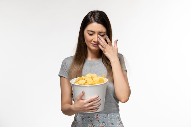 Вид спереди молодая женщина ест чипсы и смотрит фильм, плачет на белой поверхности