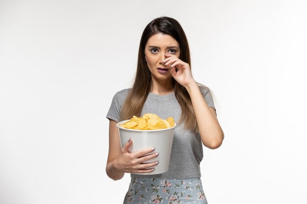 Front view young female eating cips and watching movie on light white surface