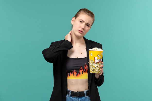 Бесплатное фото Вид спереди молодая женщина ест попкорн и смотрит фильм на синей поверхности