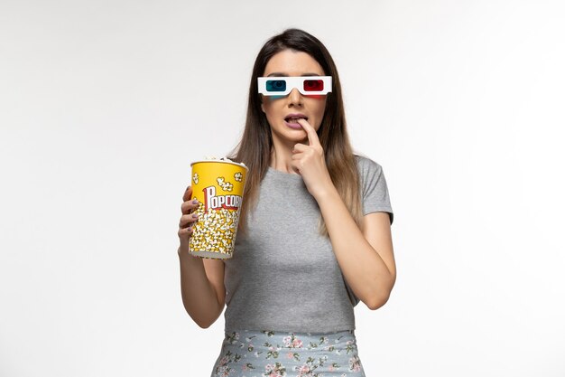 Front view young female eating popcorn package and watching movie in d sunglasses on white surface