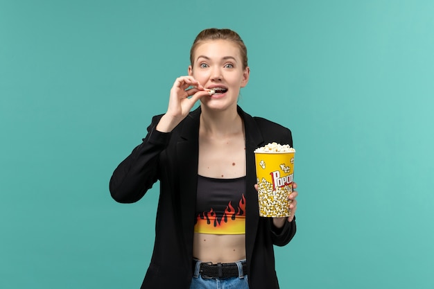 Free photo front view young female eating popcorn and watching movie on blue surface