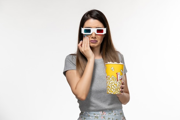 Front view young female eating popcorn and watching movie in d sunglasses on light-white surface