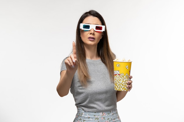 Вид спереди молодая женщина ест попкорн и смотрит фильм в солнцезащитных очках на белом столе