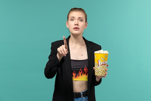 Free photo front view young female eating popcorn and watching movie on light-blue surface