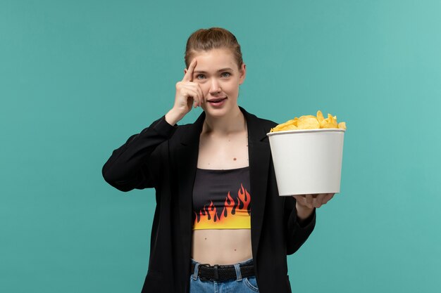 Foto gratuita giovane femmina di vista frontale che mangia patatine fritte che guarda film sullo scrittorio blu