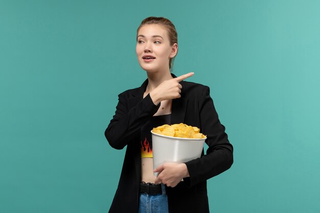 青い机の上で映画を見ているポテトチップスを食べる若い女性の正面図