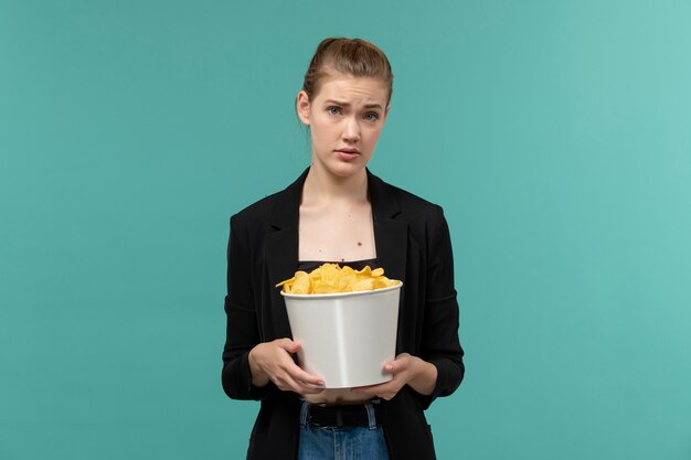 Front view young female eating potato chips and watching movie on blue surface