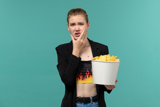 Front view young female eating potato chips watching movie on blue surface