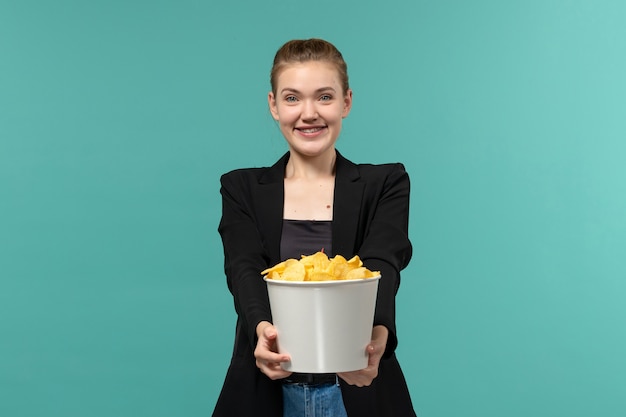 映画を見て、青い表面に笑みを浮かべてポテトチップスを食べる若い女性の正面図