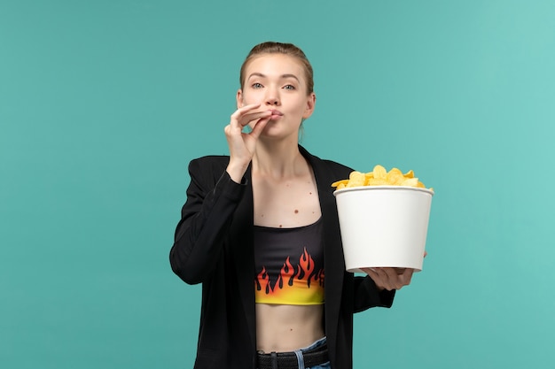 Вид спереди молодая женщина ест картофельные чипсы и смотрит фильм на синей поверхности