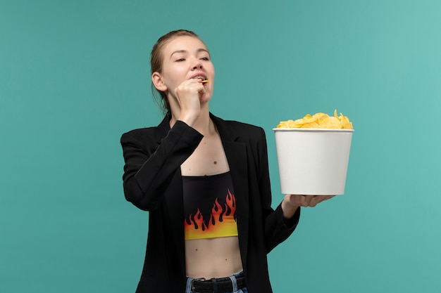 Foto gratuita giovane femmina di vista frontale che mangia le patatine fritte e che guarda film sulla superficie blu