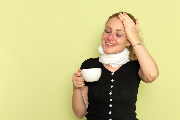 Free photo front view young female feeling very ill and sick holding cup of coffee on light-green desk sickness medicine illness health