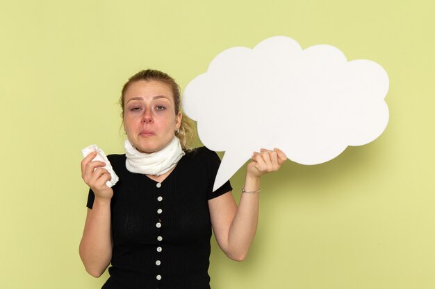 Free photo front view young female feeling very ill and sick holding huge white sign cleaning her nose on light green wall sickness medicine health illness girl