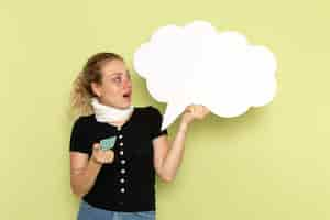 Free photo front view young female feeling very ill and sick holding huge white sign holding pills on the green desk sickness medicine health illness