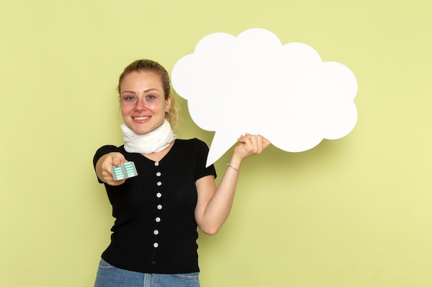 Free photo front view young female feeling very ill and sick holding huge white sign holding pills on green wall sickness medicine health illness