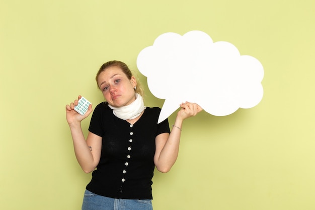 Free photo front view young female feeling very ill and sick holding huge white sign holding pills on light-green wall sickness medicine health illness