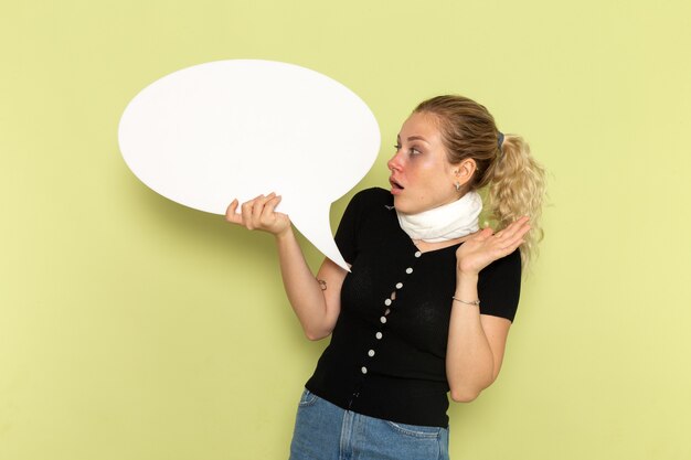 Front view young female feeling very ill and sick holding huge white sign posing on green desk sickness medicine illness health