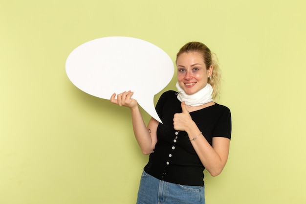 Front view young female feeling very ill and sick holding huge white sign posing and smiling on green wall sickness medicine illness health