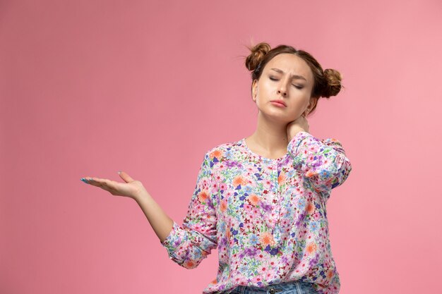 花の正面の若い女性のデザインのシャツと明るい背景に首の痛みを持つブルージーンズ