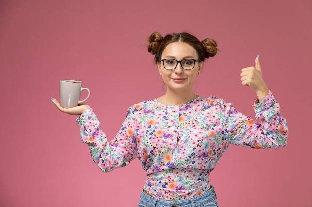 Free photo front view young female in flower designed shirt and blue jeans holding cup with smile on the pink background