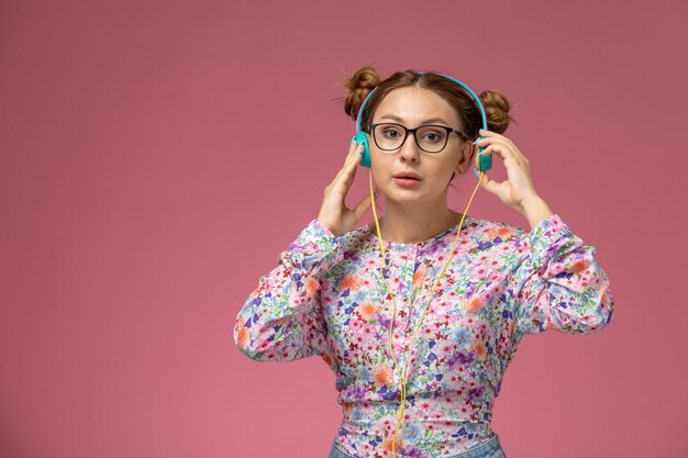 Front view young female in flower designed shirt and blue jeans listening to music with earphones on the pink background  model  female