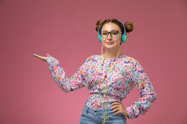 Free photo front view young female in flower designed shirt and blue jeans listening to music with earphones and smile on pink background