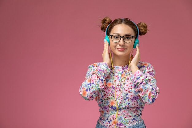 Front view young female in flower designed shirt and blue jeans listening to music with smile on her face on pink background