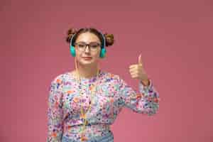 Free photo front view young female in flower designed shirt and blue jeans listening to music with smile on pink background