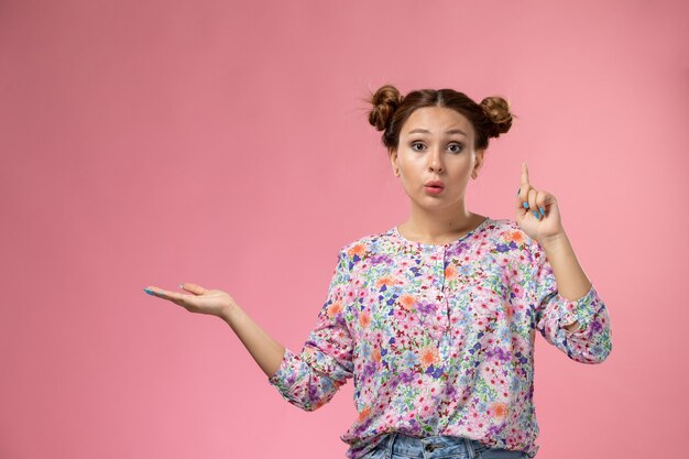 분홍색 배경에 제기 손가락으로 포즈 꽃 디자인 셔츠와 청바지에 전면보기 젊은 여성