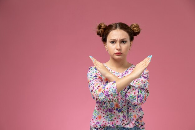 Front view young female in flower designed shirt and blue jeans showign ban sign on the pink background