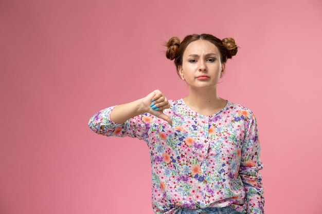 Front view young female in flower designed shirt and blue jeans showing unlike sign on pink background