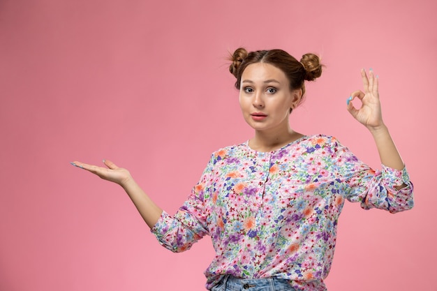 Front view young female in flower designed shirt and blue jeans smiling and posing on light-pink background 