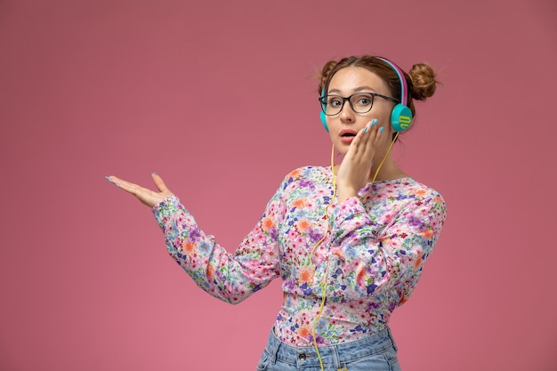 Free photo front view young female in flower designed shirt and blue jeans wearing earphones listening to music on the pink background