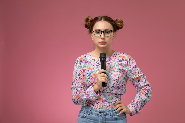 Front view young female in flower designed shirt trying to sign wiht microphone the pink background 