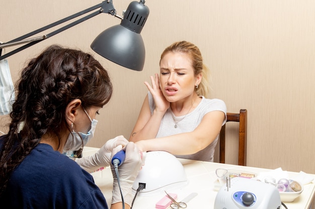 Front view young female getting her nails fixed by manicurist inside room beauty manicure nail self-care lady