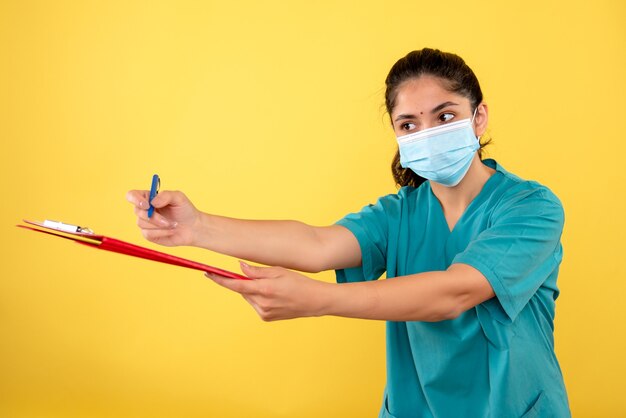 Front view of young female giving clipboard for signing on yellow wall