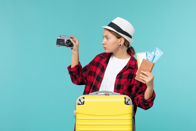 Вид спереди молодой женщины, идущей в поездку, с билетами и камерой на голубом пространстве