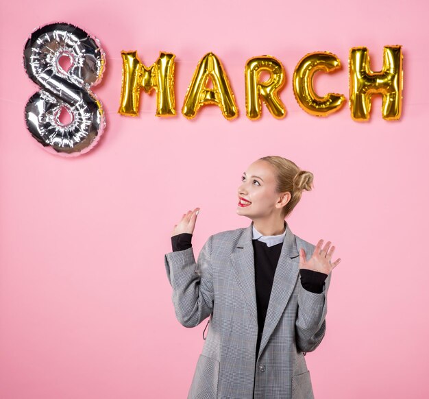 Front view young female in gray suit with march decoration on pink background color present horizontal sensual womens day equality party woman