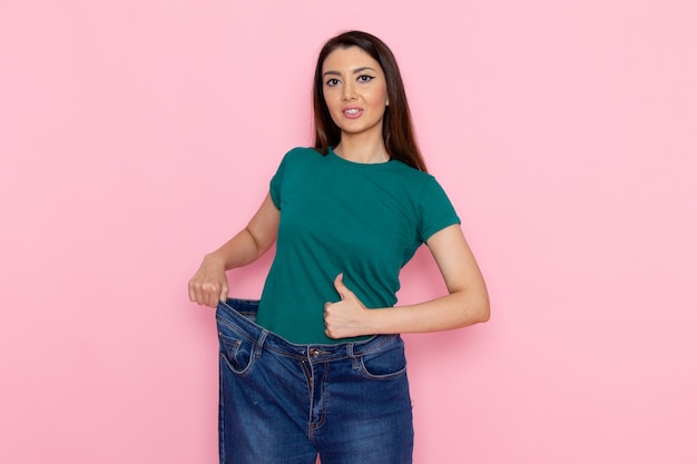 ピンクの壁のウエストスポーツ運動トレーニング美容スリムアスリートで彼女の腰をチェックする緑のTシャツの正面図若い女性