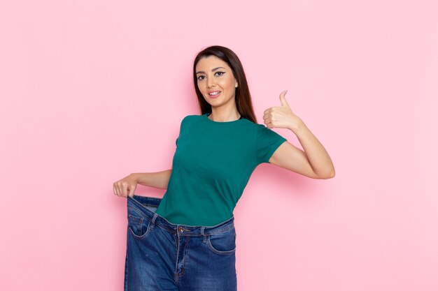 front view young female in green t-shirt checking her waist and smiling on light pink wall waist sport exercise workouts beauty slim athlete female