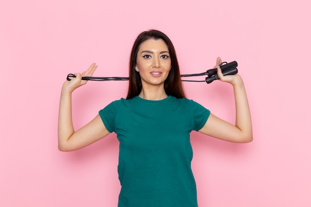 Front view young female in green t-shirt holding skipping rope on the light pink wall waist sport exercise workout beauty slim athlete