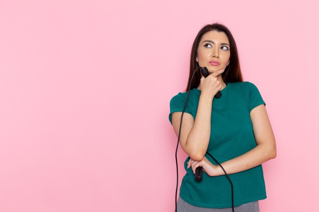 淡いピンクの壁に縄跳びロープを保持している緑のTシャツの正面図若い女性ウエストスポーツ運動トレーニング美容スリムアスリート女性