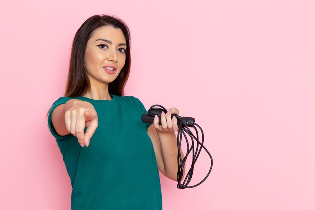 Giovane femmina di vista frontale in maglietta verde che tiene la corda per saltare sulla parete rosa chiaro vita sport esercizio allenamenti bellezza sottile atleta femminile