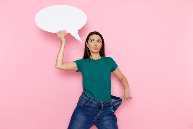 Front view young female in green t-shirt holding white sign on pink wall waist sport exercise workout beauty slim athlete