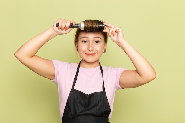 ピンクのtシャツと黒いケープのヘアブラシを緑に笑顔で髪を修正する正面の若い女性美容師